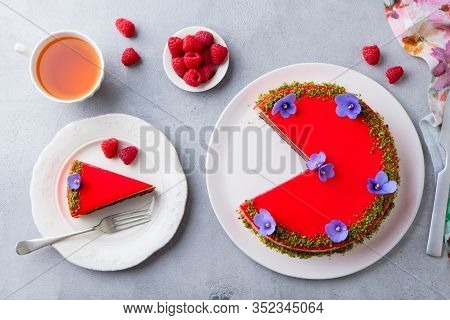 Raspberry Layerd Cake Decorated With Violet Flowers And Tea Cup. Grey Stone Background. Top View.