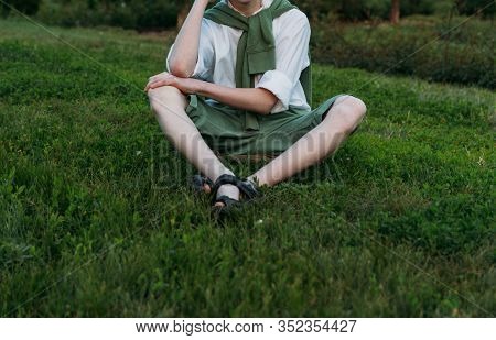 Boy In A White Shirt, Green Shorts And A Sweater Sits On Green Grass