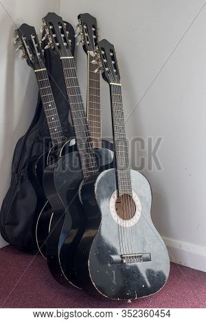 Stack Of Student Classical Acoustic Guitars In Music Room. Black Cheap Nylon String Guitars Leant On