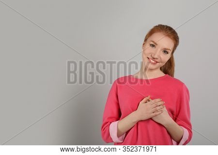 Beautiful Grateful Woman With Hands On Chest Against Light Grey Background. Space For Text