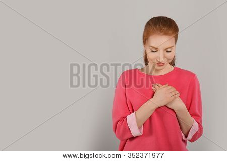 Beautiful Grateful Woman With Hands On Chest Against Light Grey Background. Space For Text
