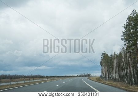 Road In Autumn Forest With Clouds In The Sky