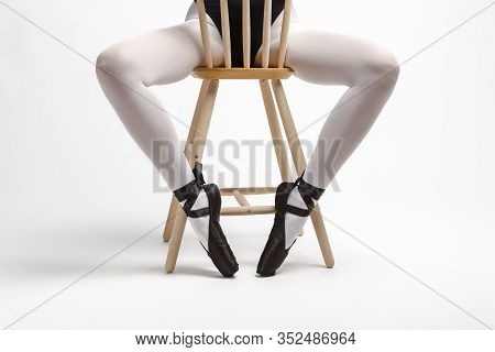 Legs Of Caucasian Ballet Dancer In Body Suit And Pointes Shoes Sitting On High Chair Against White B