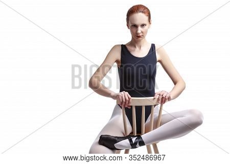 Caucasian Ballet Dancer In Body Suit And Pointes Shoes Sitting On Chair Against White Background. Ho