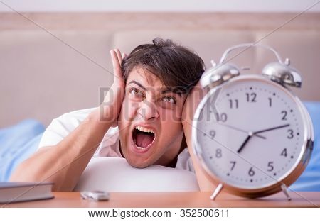 Man in bed frustrated suffering from insomnia with an alarm cloc