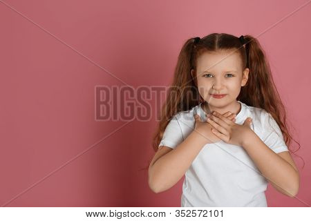 Cute Grateful Little Girl With Hands On Chest Against Pink Background. Space For Text