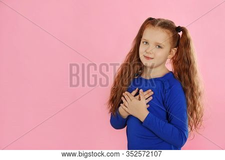Cute Grateful Little Girl With Hands On Chest Against Pink Background. Space For Text