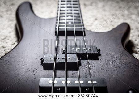 Bass Guitar With Four Strings Closeup. Detail Of Popular Rock Musical Instrument. Close View Of Dark