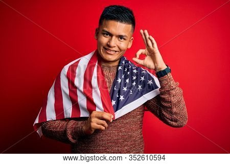 Young handsome latin patriotic man wearing united states of america falg doing ok sign with fingers, excellent symbol