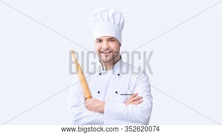 Cheerful Baker Man Holding Dough Rolling Pin Smiling To Camera Standing On White Studio Background. 