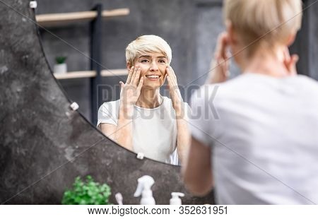 Attractive Mature Lady Touching Perfect Smooth Face Skin Making Daily Skincare Routine Standing In B