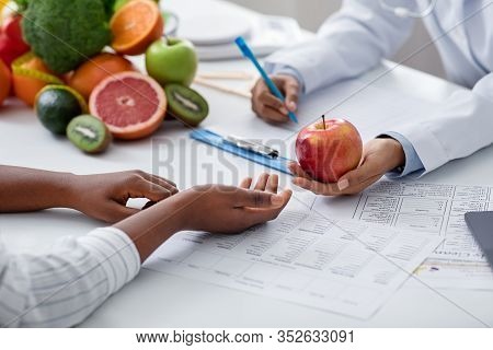 Doctor Dietologist Giving Apple To Afro Woman Patient During Session, Close Up