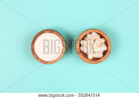 Collagen In Capsules And In Powder In Two Wooden Bowls On Pastel Blue Background