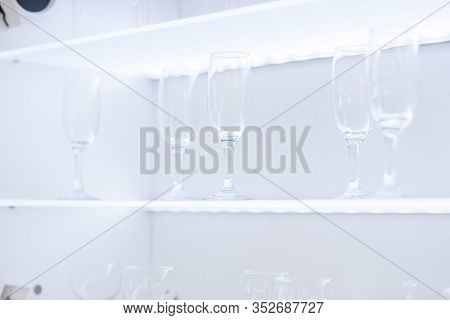 Clean Wine Glasses And Champagne Flutes Upended On A White Wooden Shelf In A Kitchen Or Bar