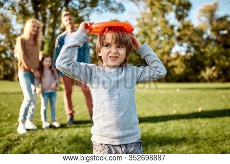 Portrait Of Happy Family Of Four Going To Play With Disc On A Green Meadow With Grass. Focus On Cute