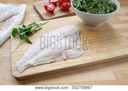 Raw Plaice Fillet, Tomatoes And A Bowl Of Mashed Celery And Arugula On A Wooden Kitchen Board, Cooki