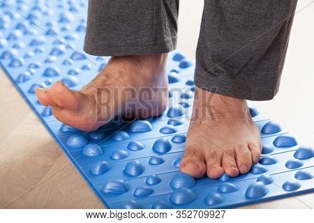 man doing flatfoot correction gymnastic exercise walking on massage mat at home