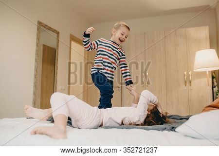 Caucasian Boy Playing With His Bigger Sister Lying On The Bed And Smiling Cheerfully