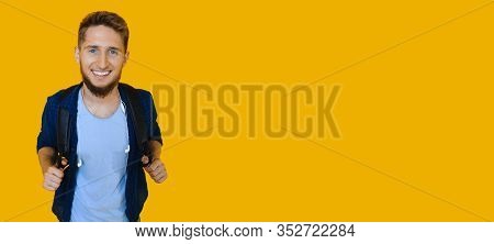 Ginger Caucasian Student Posing With A Bag On His Shoulders While Smiling Aside On A Yellow Wall Wit