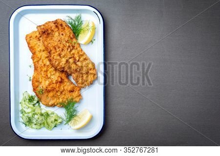 Traditional deep fried Wiener schnitzel from veal topside with cucumber salad and lemon slices offered as top view on a white tray with copy space right 