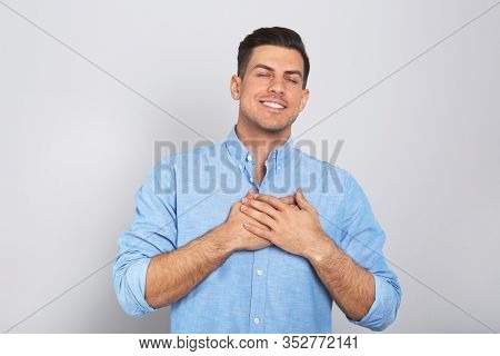 Handsome Grateful Man With Hands On Chest Against Light Grey Background