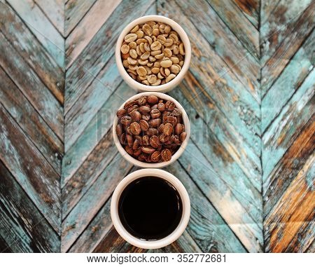 Green Raw Beans, Roasted Coffee Beans And Black Coffee In Three White Cups On Turquoise Wooden Backg