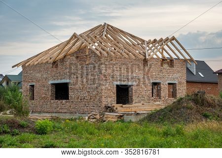 Building Site With Unfinished Brick House With Wooden Roofing Frame For Future Roof Under Constructi