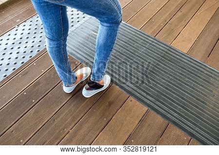 Female Legs In Denim Jeans Pants And Light Summer Sneakers Standing On Wooden Floow.