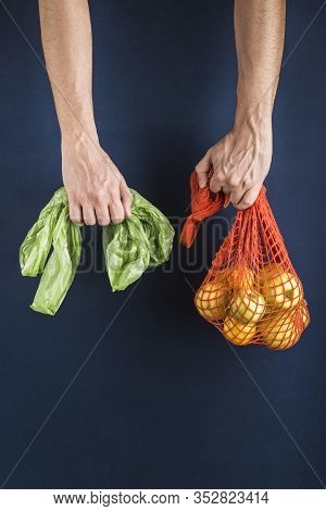 Apples And Lemons In An Orange String Bag In One Man's Hand In Another Plastic Bag On A Dark Blue Ba
