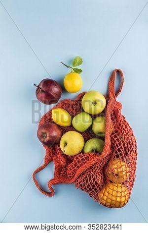 Apples And Lemons In An Orange String Bag On A Blue Background. Top View. Concept Of Life Without Pl