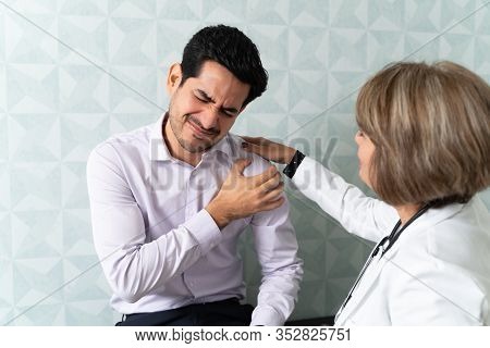Senior Female Doctor Examining Mid Adult Man Suffering From Joint Pain In Clinic