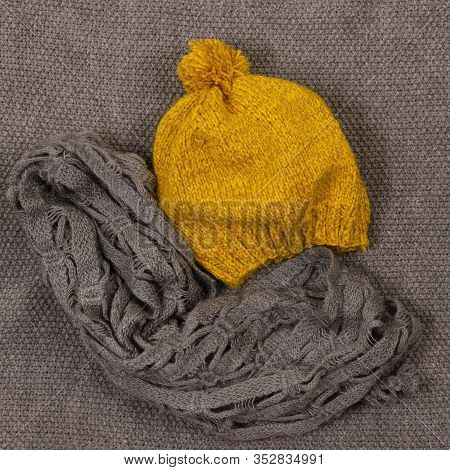 Yellow Mustard Beret With Pampon And Gray Scarf On A Gray Knitted Background