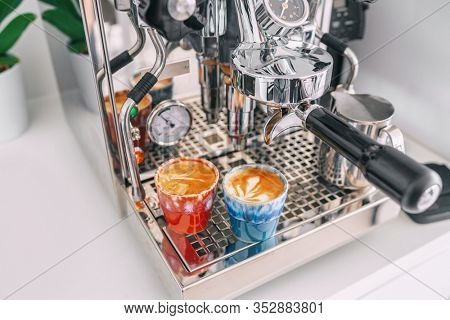 Two macchiato shots in espresso cups on coffee machine at home - white apartment kitchen, modern interior lifestyle.