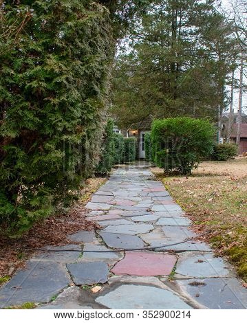 A Multi-colored Stone Path Leading Up To The Front Door Of A Home With Trees And Bushes On The Sides