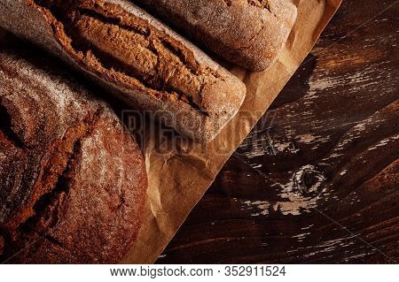Rye Bread And A Loaf On Paper, Lying On A Wooden Table. Illuminated By Warm Side Sunlight. Concept F