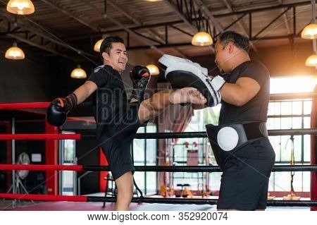 Asian Kick Boxer Kicking Professional Trainer In Boxing Studuim In The Background At Fitness Gym. Bo