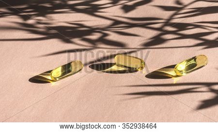 Oil Yellow Gelatin Capsules On Pink Background With Flower Shadow, Vitamins And Antioxidant Concept 