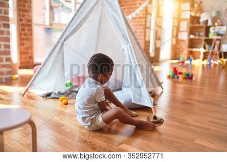 Beautiful african american toddler putting on shoes outside tipi at kindergarten