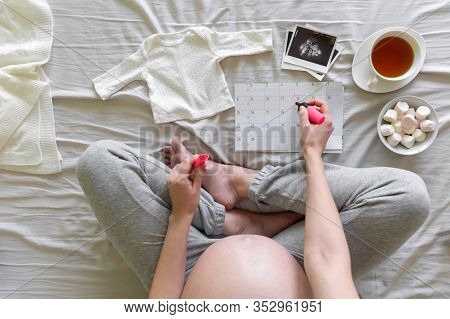 Top Vew Of Expecting Pregnant Woman Notes The Date Of Birth On The Calendar At Home, Pregnancy And B