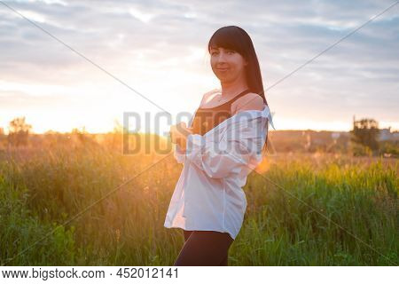 Brunette Woman In White Blouse With Baldric On Summer Field On Sunset. Peaceful Time. Millennial Gen