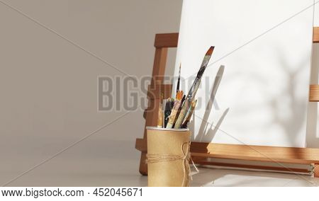 Empty copy space canwas on wood easel and paintbrush in artistic workshop interior. 
