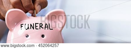 Person Saving Money For Funeral By Inserting Coin In Piggy Bank With Funeral Text