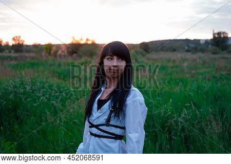 Young Woman In Baldric On The Summer Field On Sunset Or Sunrise. Peaceful Calm Female. Trendy Clothe
