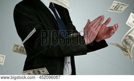 Close-up of a young businessman claping hand with flying dollars banknotes isolated over gray background