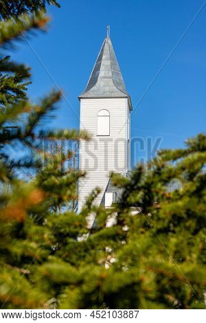 Vertical View To White Church Tower With Metal Roof Through Green Spruce Branches.  Lutheran Church 