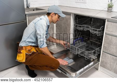 Process Of Dishwashing Machine Installation. Young Service Man Setting Up Dishwasher In New Stylish 