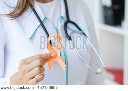 Close Up Of A Doctor Holding And Showing Orange Awareness Ribbon In Her Hands