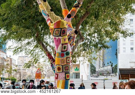 Netanya, Israel - February 7, 2022: Colorful Crochet Knit On A Tree Trunk Yarn Bombing. Patchwork Kn
