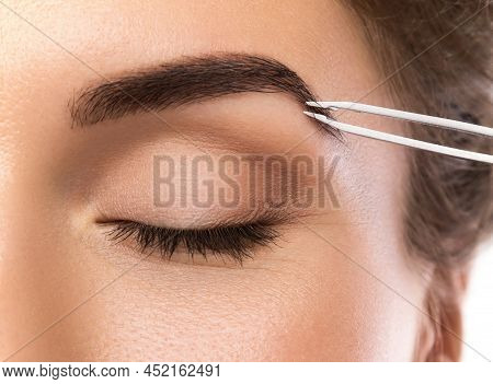 Close-up Of Female Face And Eyebrow With Tweezers