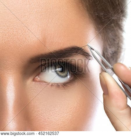 Close-up Of Female Face And Eyebrow With Tweezers